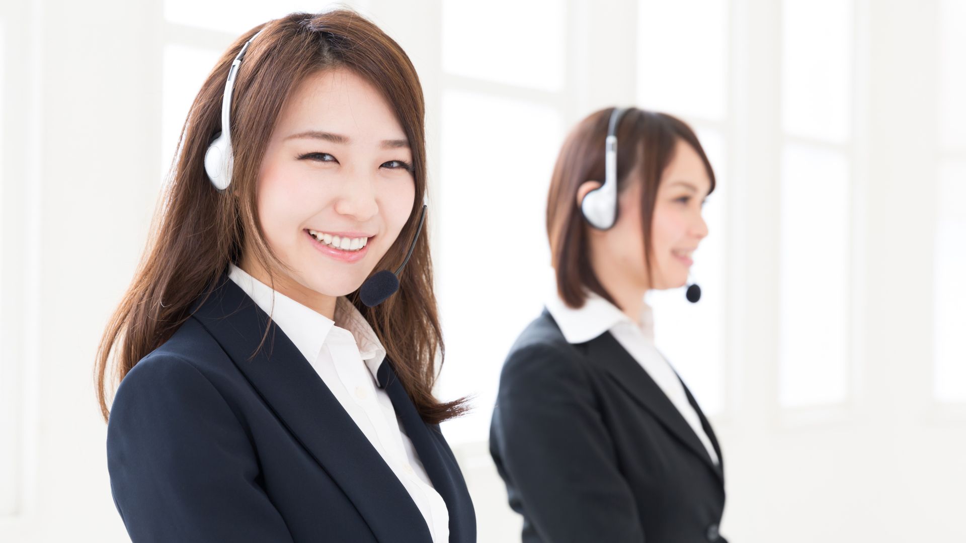 コールセンターの女性オペレーターたちが笑顔で対応している背景画像